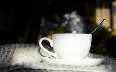 A sunlit coffee cup stands on a sweater. Background - bookshelves