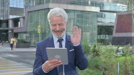 Old Businessman Talking on Video Call on Tablet while Walking on the Street