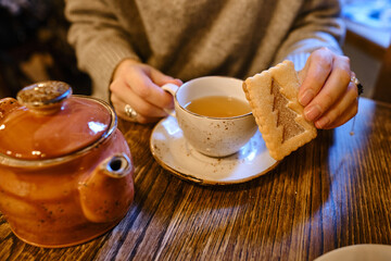 A woman with a cup of tea sits in a cozy cafe with a sweet cookie in her hands. Delicious traditional desserts