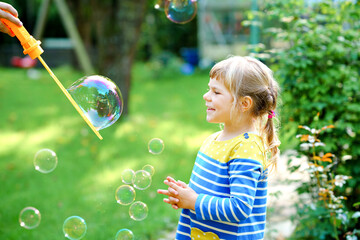 Happy little blonde preschool girl having fun with blowing soap bubble blower. Cute child playing on sunny summer day. Happy active funny healthy kid. Activity for children.