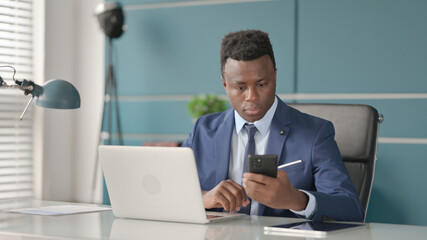 African Businessman using Smartphone while using Laptop in Office 