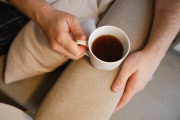 A cup of tea or coffee in the hands of a man. A man drinks hot tea in the morning. Enjoy the comfort of home. White cup close-up in the hands of a man