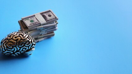 Business minded concept. Brain model and stack of money on blue background with copy space