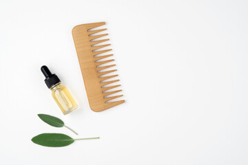 Hair care set. Wooden comb, hair oil. White background, top view, copy space.