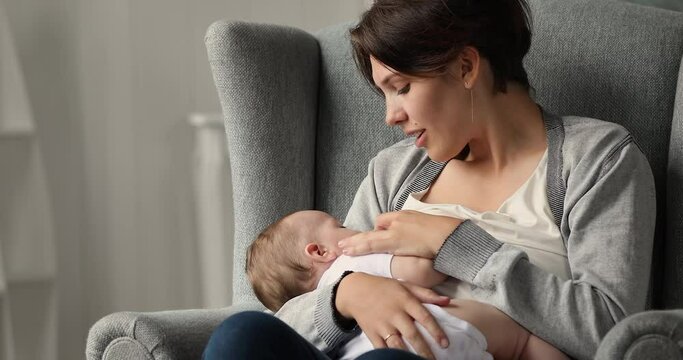 Young smiling woman sit on cozy armchair at home breastfeeding her newborn cute baby. Lactation, source of nutrition for growth and good development of children, moments of happy motherhood concept