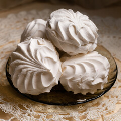 White vanilla marshmallows are lying on a small plate on a lace napkin. Square image.