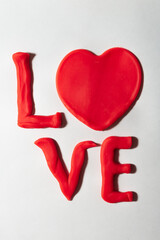 The word "Love" is made of red plasticine on a white background. Vertical photo. Valentine's Day card.