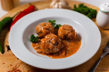 Meat balls in sauce on a white plate on a wooden background