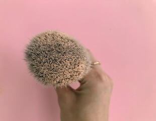 brush in powder on a pink background. brush in hand of a make-up artist. Mineral and matte beige...