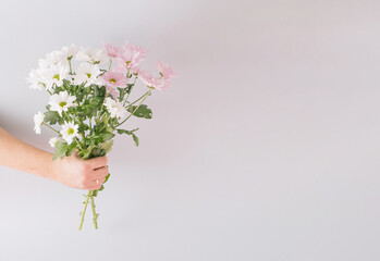 Creative spring arrangement made of a bouquet of flowers in hand on a gray background. Minimal concept with copy space.