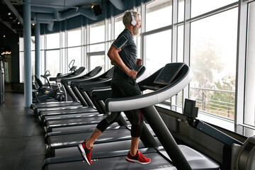 Naklejka na ściany i meble Determined elderly sportsman jogging on treadmill at gym