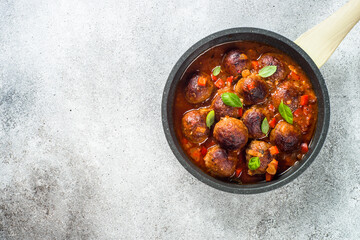 Meatballs in tomato sauce and basil at light stone table. Top view with copy space.