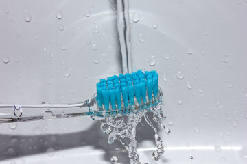 A blue toothbrush under running water. Teeth cleaning.