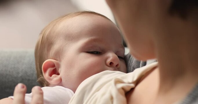 Close up view, face of adorable newborn sucks mothers milk. Woman sit indoors breastfeeding her sweet son or daughter. Lactation of child for healthy growth and development. Happy maternity concept