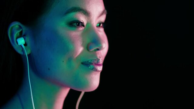 Attractive Young Asian Woman Illuminated By Neon Lights Listening Music In Earphones