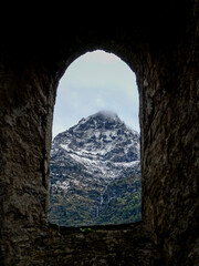 View trough a medieval window of a castle in Switzerland on a snow covered mountain with cloudy sky