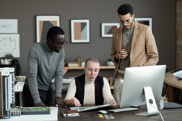 Group of contemporary intercultural architects or designers discussing papers with interior photos by workplace
