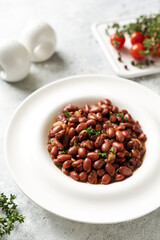 Stewed red beans with onion and thyme in tomato sauce in a white plate on the kitchen table closeup