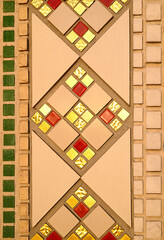 A fragment of a geometric repeating pattern from a ceramic mosaic on the wall of a Catholic church. Gold, red, beige and green mosaic tile.
