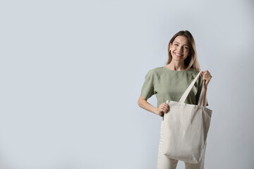 Happy young woman with blank eco friendly bag on light background. Space for text