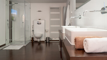 Modern bathroom in white and brown with two sinks, toilet, shower and wooden furniture