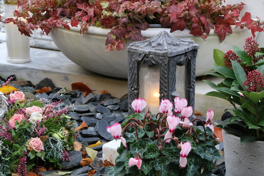 Herbstliche Grabbepflanzung eines Urnengrabes an einem Friedhof in Österreich zu Allerheiligen, Herbstpflanzen wie das Alpenveilchen bei Kerzenschein einer Friedhofslaterne, Trauer, Gedenken
