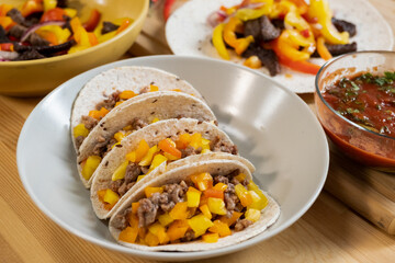 White porcelain plate with traditional mexican taco surrounded by homemade tomato sauce and vegetable stew