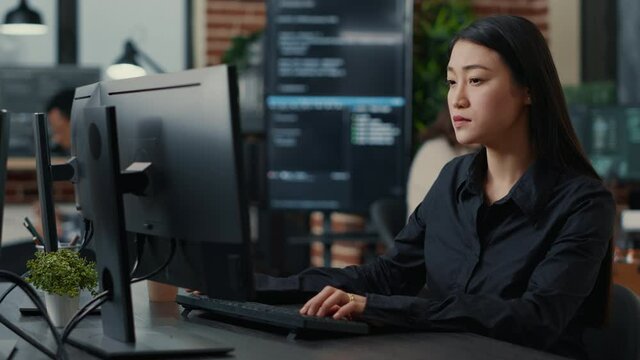 Portrait of smiling asian programer focused on writing code sitting at desk in software development office. System engineer concentrating on creating algorithm for it startup company.