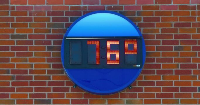 Outdoor digital LED clock and thermometer displaying time and temperature on a brick wal