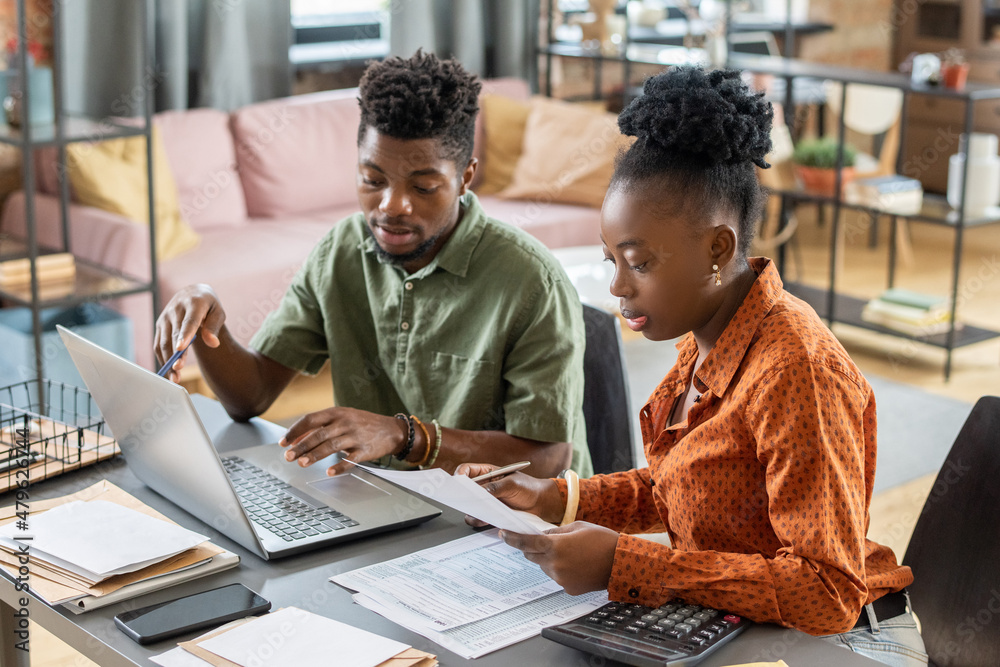 Poster young confident businessman making presentation to african female with papers while checking online 