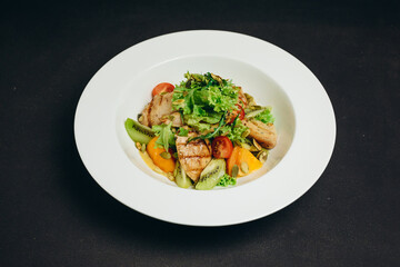 There is a dish that includes some kiwi, tomatoes, green and meat.
