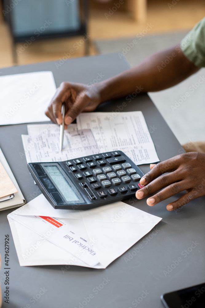 Aufkleber Hands of African man checking data in unpaid bills and tax payment forms while pointing at one of papers on table