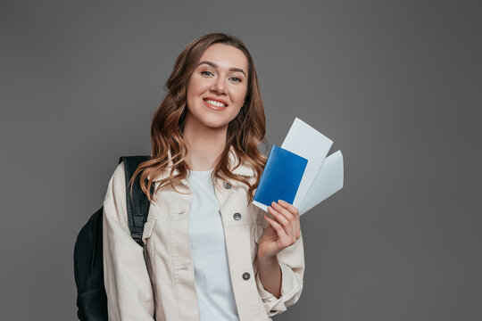 sstudy abroad concept. student girl holding backpack, book, notebook, passport isolated on a dark grey background, copy space, immigration,
