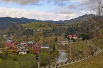 Naklejka premium Magnificent panorama of a picturesque mountain village in autumn. Autumn mountain landscape in the Ukrainian Carpathians - yellow and red trees combined with green needles. Panoramic view.