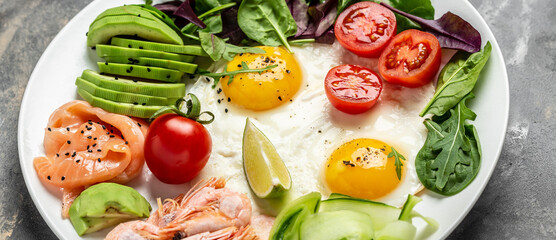 Ketogenic breakfast. Keto low carb salmon, boiled shrimps, prawns, fried eggs, fresh salad, tomatoes, cucumbers and avocado. Top view