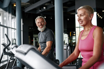 Fototapeta na wymiar Seniors workout in gym. Smiling man looking at woman