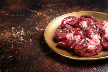 Raw Beef kidney, fresh sliced offal meat on plate. Dark background. Top view. Copy space