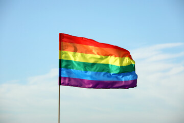 Bright LGBT flag against blue sky with clouds