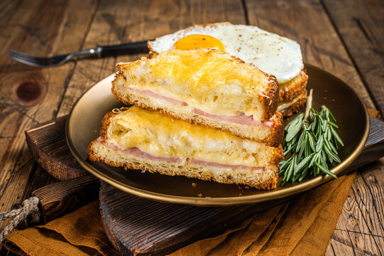 Croque monsieur and croque madame sandwiches with sliced ham, melted emmental cheese and egg, French toasts. Wooden background. Top view