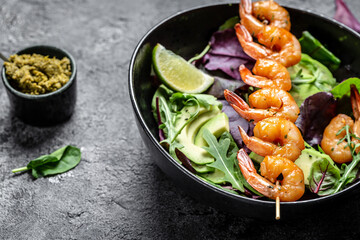 Vegetarian vegetable low carb lunch bowl with avocado, fresh salad, grilled shrimps and pesto sauce. Healthy diet seafood concept. Top view