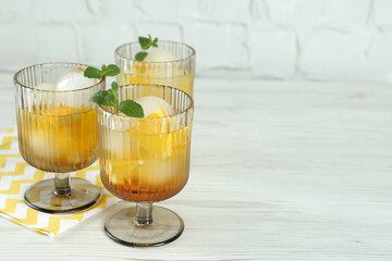 Delicious cocktails with orange, mint and ice balls on white wooden table, space for text