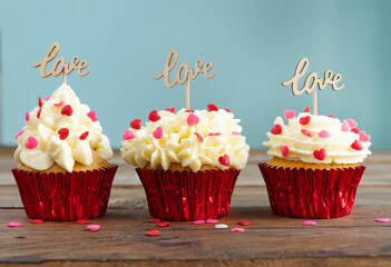 Three cupcakes with red topping decoration and a wooden sign with the word LOVE on a wooden background. Copy space.