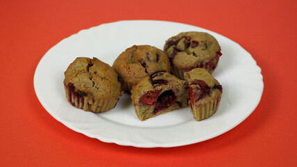 four muffins made of rice flour, yogurt, cherries and pumpkin oil lie on a gray plate on a red background, side view. gluten-free homemade cakes