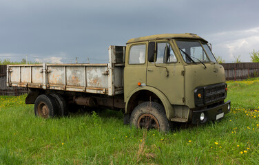 An old lorry in a field among the green grass. Military cabin color. Rusty body.