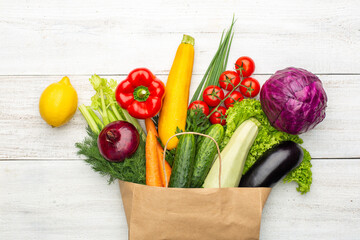 Set of vegetables and herbs in a paper bag on a white wooden background. Healthy Vegetarian Food.