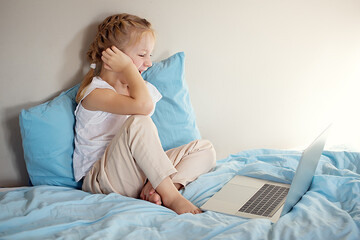 A cute girl sitting on the bed is watching something on a laptop. The concept of education