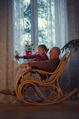 grandfather sitting in a chair and reading a fairy tale to his granddaughter on Christmas eve