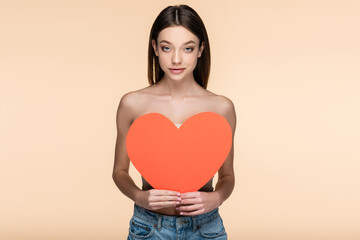 happy woman with bare shoulders covering body with red paper heart isolated on beige