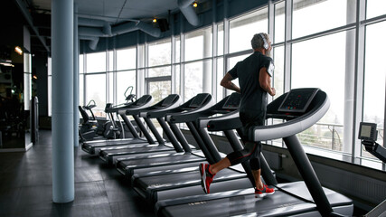 Man listening to music via headphones and running on treadmill