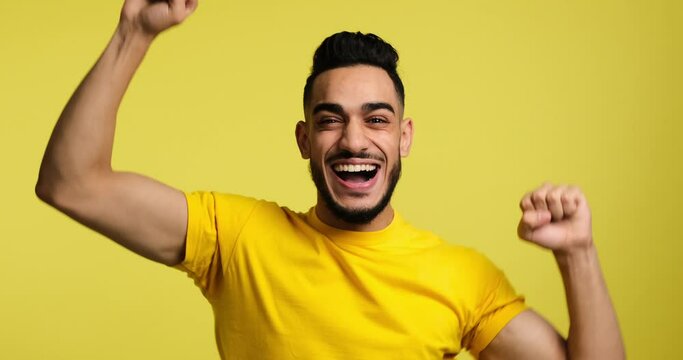 Enthusiastic young man celebrating success over yellow background